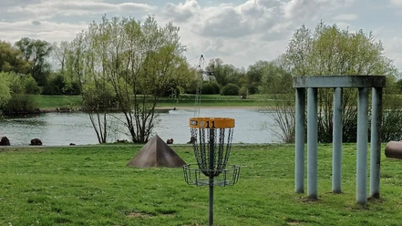 Ein Discgolf-Korb auf einer grünen Wiese direkt am Ufer des Salzgittersees.