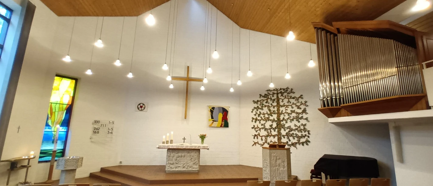 Friedenskirche_Salzgitter-Lebenstedt_HD_16zu9.jpg Heller Innenraum der Friedenskirche mit Altar, Kreuz, Orgel und Sitzreihen.