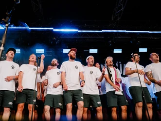 Grüngürtelrosen & Freunde - Sommergarten Gruppe von Männern in weißen Shirts singt gemeinsam auf einer beleuchteten Open-Air-Bühne