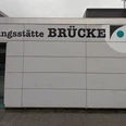 Bruecke_Fredenberg_HD_16zu9.jpg Eingang zur Begegnungsstätte Brücke mit großem Schriftzug an der grauen Fassade.