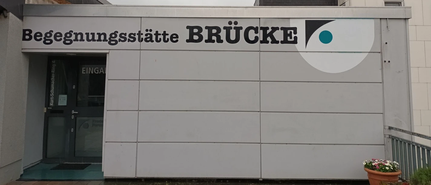 Bruecke_Fredenberg_HD_16zu9.jpg Eingang zur Begegnungsstätte Brücke mit großem Schriftzug an der grauen Fassade.