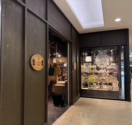 Sostrene Grene Dunkle Holzfassade eines Søstrene Grene Geschäfts mit offenem Eingang und Schaufenster.