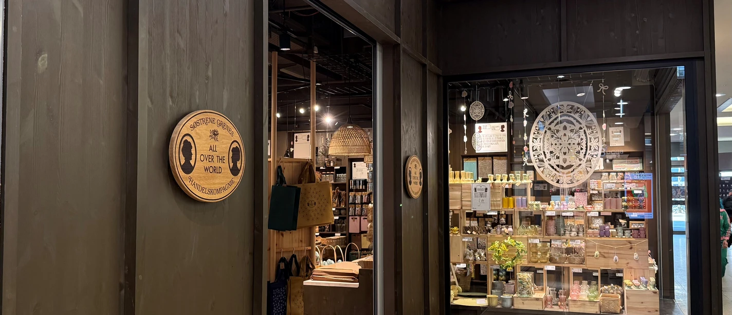 Sostrene Grene Dunkle Holzfassade eines Søstrene Grene Geschäfts mit offenem Eingang und Schaufenster.