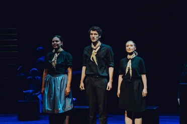 Die Weiße Rose, Hans, Sophie Inge Three performers in dark clothing stand on a stage and sing in the spotlight.