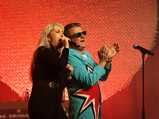 Linus talent sample Two stage artists sing and perform in front of red lights, a microphone stands at the side.