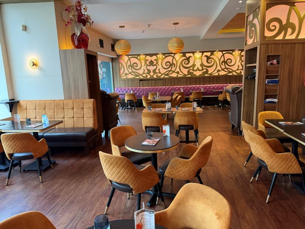 Cup&Cino 2026 Ein einladender Innenraum mit dunklen Holztischen, senfgelben Sesseln und lila Sitzbänken.