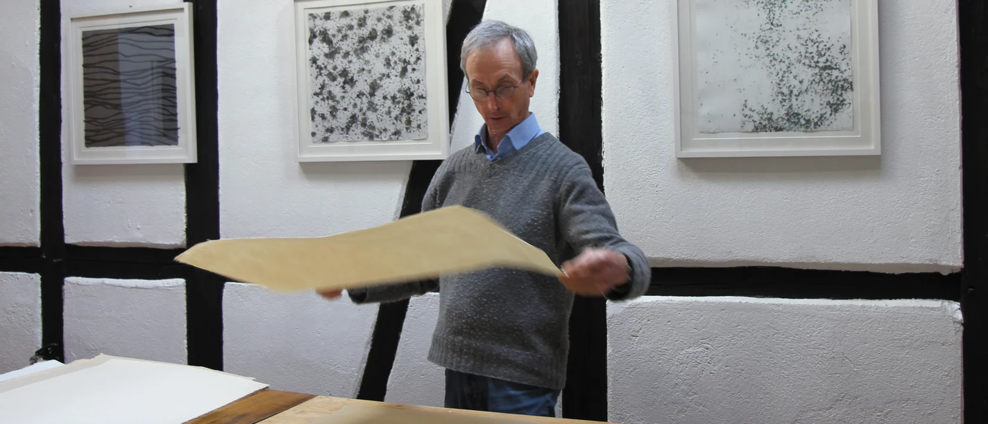 Papier sortieren Person sortiert handgeschöpftes Papier an einem Tisch vor gerahmten Bildern.