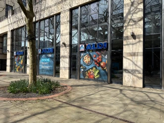 Aldi Nord Wolfsburg (in den Museums Arcaden) Moderne Gebäudefassade einer Aldi-Filiale mit großen Schaufenstern und Lebensmittelwerbung.