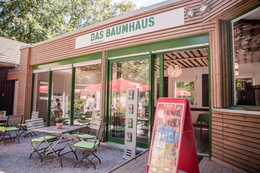 Das Baumhaus - Bistro im Waldkletterpark Bistro 'Das Baumhaus' im Waldkletterpark: Holzfassade, grüne Details, Tische und Stühle auf Kies.