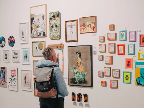 Urban Wildcard Art im Studio 40 Köln Person betrachtet vielfältige Kunstwerke an einer hellen Ausstellungswand.
