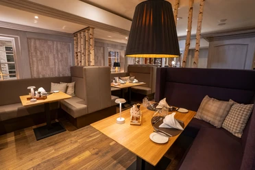 Huxori Stube.jpg Restaurantbereich mit Holztischen, gepolsterten Sitznischen und warmem Licht