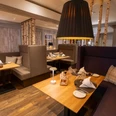 Huxori Stube.jpg Restaurantbereich mit Holztischen, gepolsterten Sitznischen und warmem Licht
