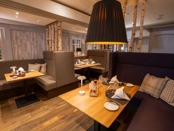 Huxori Stube.jpg Restaurantbereich mit Holztischen, gepolsterten Sitznischen und warmem Licht