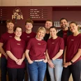 Das Team vom Café FRIDA in Büsum Acht Personen vor einem Tresen in roten Shirts.