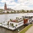 Freigut Bootshaus - exterior view Boat with terrace on River Main, Frankfurt Cathedral behind