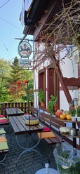 Kräutercafé Außenbereich mit Holzbänken, farbigen Sitzkissen, Kürbissen, Pflanzen und einem Brauereischild.
