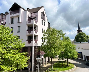 Ferienwohnung Der Gerber in Hilden Mehrstöckiges helles Gebäude mit Balkonen und grünen Bäumen in Hilden, im Hintergrund ein Kirchturm.
