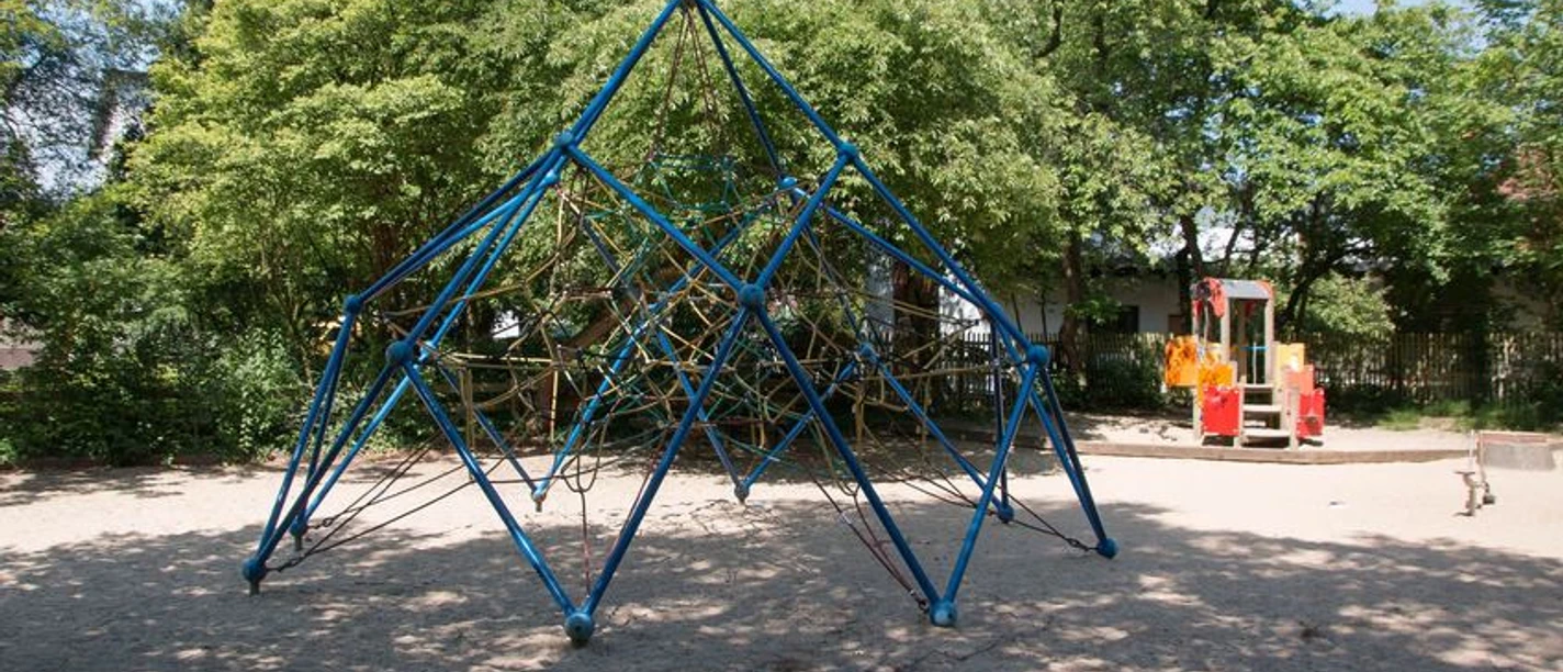 Seilpyramide auf dem Sandspielplatz umgeben von Bäumen