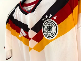Trikot der deutschen Nationalmannschaft Weißes Fußballtrikot mit schwarz-rot-goldenem Muster und DFB-Emblem mit vier Sternen