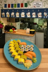 Sushi-Teller mit Lachs-Nigiri und Maki vor Theke mit Winkekatzen-Dekor