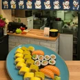 Sushi-Teller mit Lachs-Nigiri und Maki vor Theke mit Winkekatzen-Dekor
