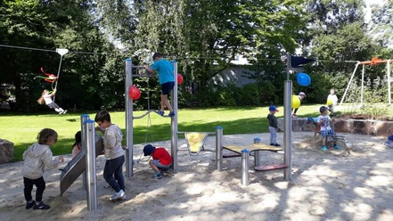 Einweihung bei strahlendem Sonnenwetter (1)_WEB.jpg Kinder spielen im Sandbereich auf dem Spielplatz und ein weitere Kind saust im Hintergrund mit der Seilbahn über den Spielplatz