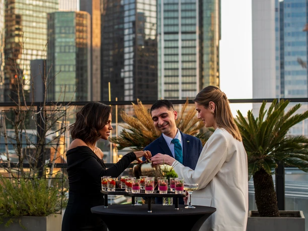 Sofitel Frankfurt Opera - Gäste Drei Personen an Stehtisch mit Skyline Frankfurt im Hintergrund