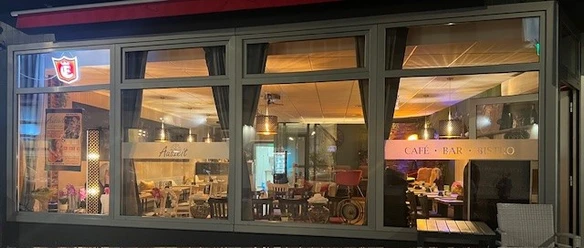 cafe-auszeit.jpg Beleuchtetes Café Auszeit mit Sitzplätzen im Innenraum und Terrasse am Abend