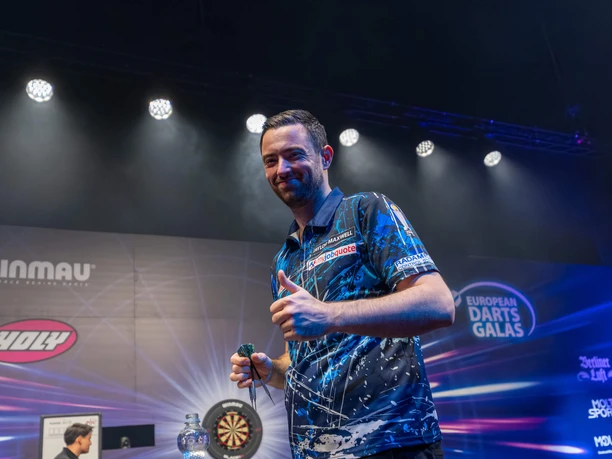 Winamax Cologne World Darts Gala Darts players on illuminated stage with thumbs up in front of tournament backdrop