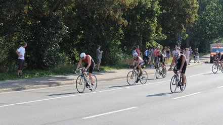 Triathlon_Salzgitter_HD_16zu9.JPG Triathleten auf Rennrädern fahren auf einer Straße an Zuschauern am Rand vorbei.