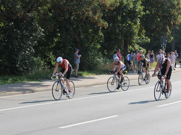 Triathlon_Salzgitter_HD_16zu9.JPG Triathleten auf Rennrädern fahren auf einer Straße an Zuschauern am Rand vorbei.