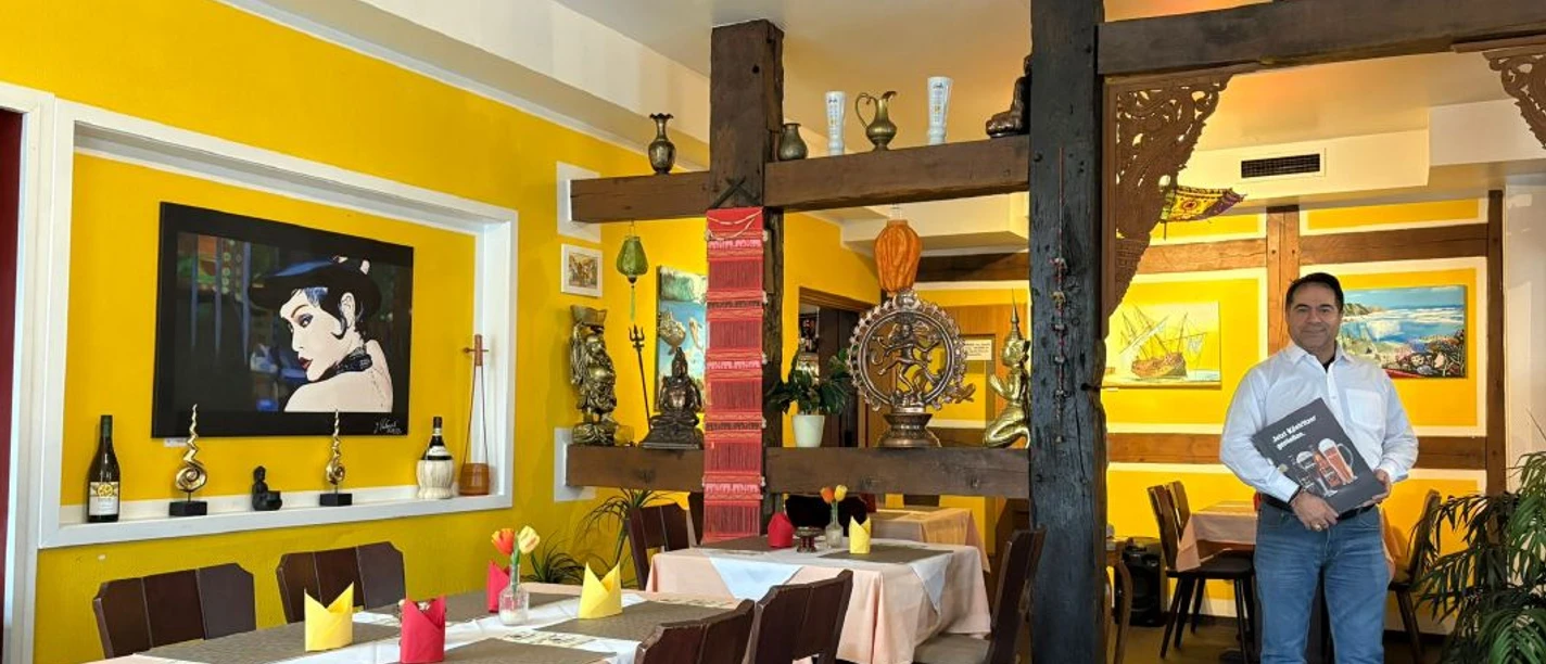 lion-restaurant.jpg Innenraum eines indischen Restaurants mit gelben Wänden, gedeckten Tischen und Inhaber