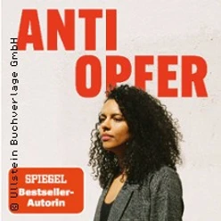 Frau mit lockigem Haar vor weißer Wand unter großem roten Buchtitel Anti Opfer