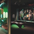 Blick in die Ausstellung - GRASSI Museum für Völkerkunde Blick in einen Ausstellungsraum des GRASSI Museums für Völkerkunde mit einer Sitzmöglichkeit und verschiedenen Vitrinen, in denen Ausstellungsstücke zu Klanggeschichten von den Andaman und Nicobar Islands präsentiert werden.