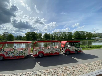 Bimmelbahn-Weser-Huxarium Gartenpark Höxter gGmbH.jpg Bimmelbahn am Weserufer in Höxter mit Blick auf Fluss