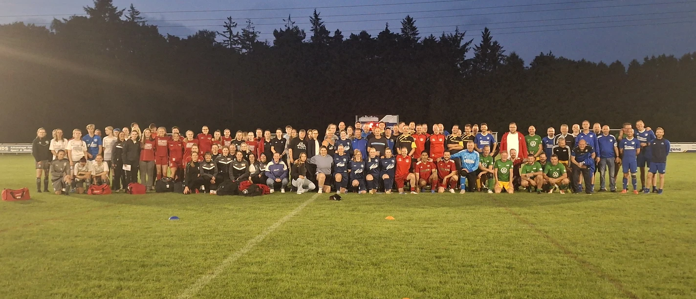 20250718_222232.jpg Fußballmannschaften posieren abends auf dem beleuchteten Rasenplatz für ein Gruppenfoto.