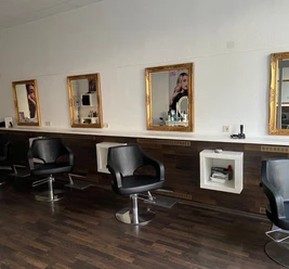 Haarkunst Friseursalon Friseursalon mit schwarzen Friseurstühlen, Spiegeln mit Goldrahmen und dunklem Holzboden.