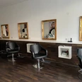 Haarkunst Friseursalon Friseursalon mit schwarzen Friseurstühlen, Spiegeln mit Goldrahmen und dunklem Holzboden.