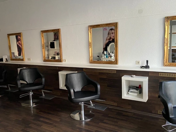 Haarkunst Friseursalon Friseursalon mit schwarzen Friseurstühlen, Spiegeln mit Goldrahmen und dunklem Holzboden.