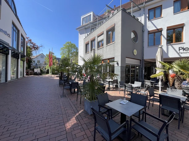 Außenterrasse des Eiscafés mit Tischen, Stühlen und Palmen in Fußgängerzone