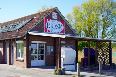 Kiosk Trockenstrand Upleward Backsteinkiosk mit auffälligem Schild, einer weißen Tür und Strandkörben unter dem Vordach.