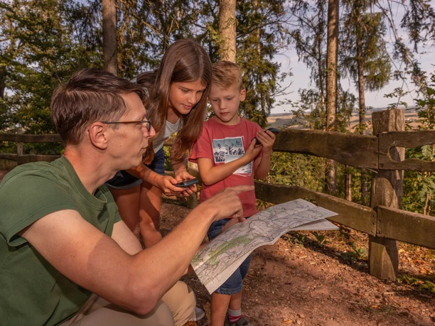 Ein Mann und zwei Kinder betrachten auf dem Rochlitzer Berg eine Wanderkarte, die der Mann geöffnet in der Hand hält. Sie suchen gemeinsam nach dem richtigen Weg ihrer Wanderung.