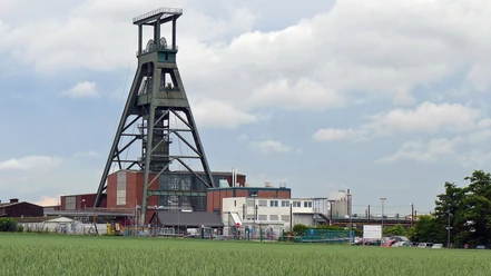 Schacht Konrad Salzgitter_HD_16zu9.jpg Hoher stählerner Förderturm der Anlage Schacht Konrad hinter einem grünen Feld.