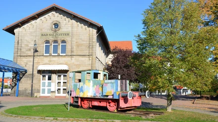 Bahnhof_SZ-Bad_HD_16zu9.JPG Bahnhof Salzgitter-Bad aus Stein. Davor steht eine bunte Lokomotive.