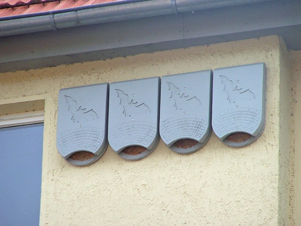 Fledermaushotel an der Hauswand Graue Fledermauskästen an einer gelben Hausmauer