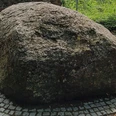 Brunnen_Irenenquelle_SZ-Bad_HD_16zu9.jpg Ein großer, runder Findling ruht auf einem gepflasterten Platz, umgeben von einem Gitterzaun.