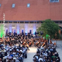 Open-Air-Orchester vor beleuchteter Fassade, Publikum sitzt dicht gereiht im Innenhof.