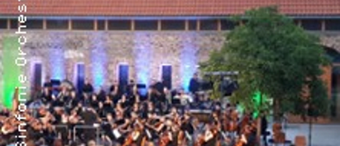 Open-Air-Orchester vor beleuchteter Fassade, Publikum sitzt dicht gereiht im Innenhof.