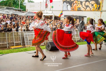 Lateinamerikanisches Wochenende an der Südbrücke Köln Tanzgruppe in farbenfroher Tracht auf Bühne vor großem Publikum beim Festival