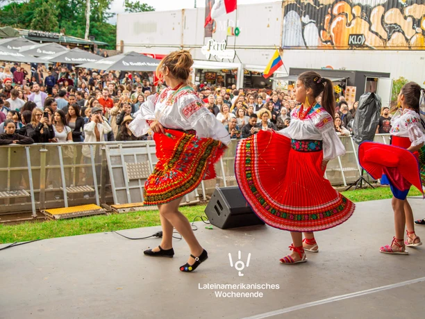 Lateinamerikanisches Wochenende an der Südbrücke Köln Tanzgruppe in farbenfroher Tracht auf Bühne vor großem Publikum beim Festival